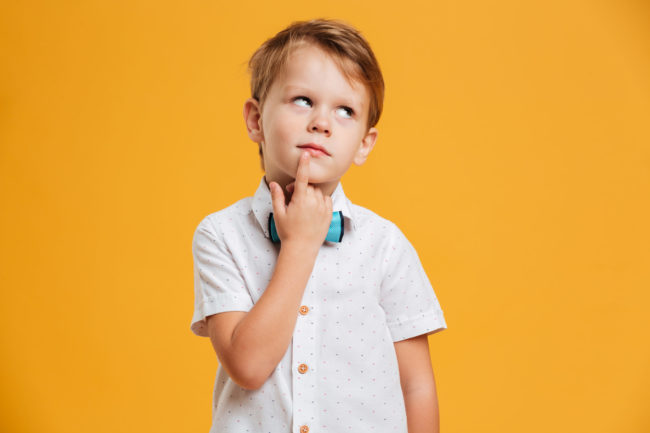A little boy thinking with one finger on lips and looking upwards